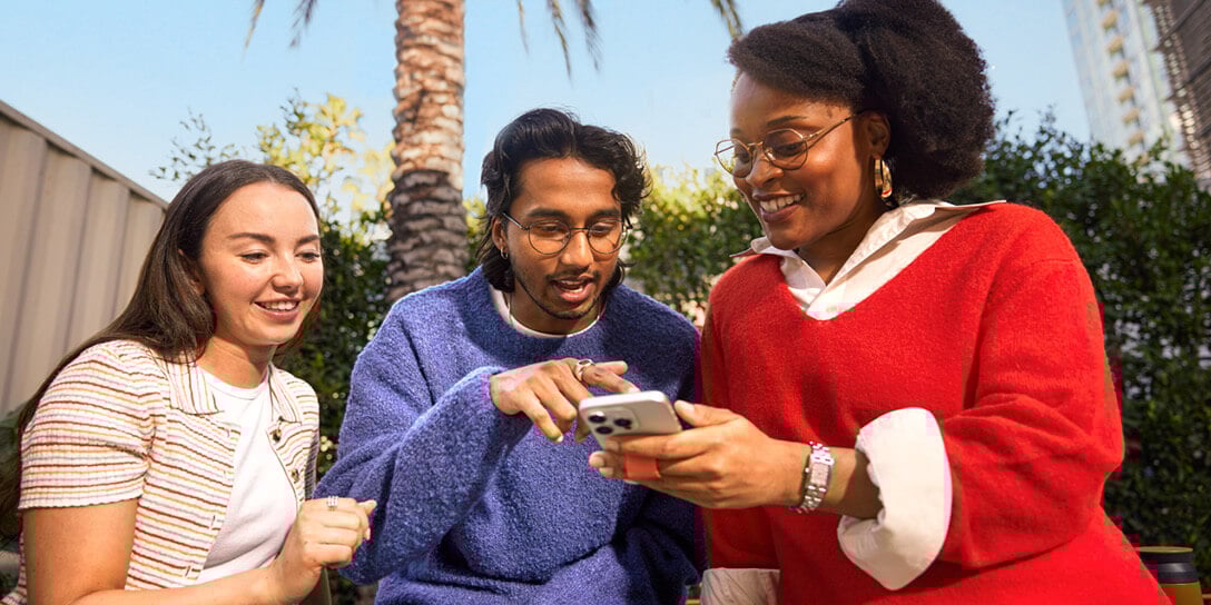 Three people smile while looking at a phone together, symbolizing the benefits of using online customer feedback forms.